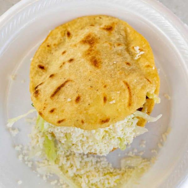 A Giliberto's Mexican Taco Shop gordita filled with shredded cheese and lettuce on a white plate.