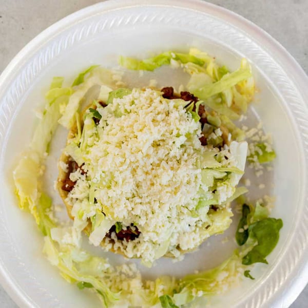 A Giliberto's Mexican Taco Shop tostada, topped with shredded lettuce and crumbled white cheese.