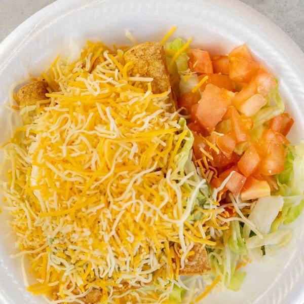 A Giliberto's Mexican Taco Shop dish with shredded cheese, lettuce, and diced tomatoes in a white bowl.