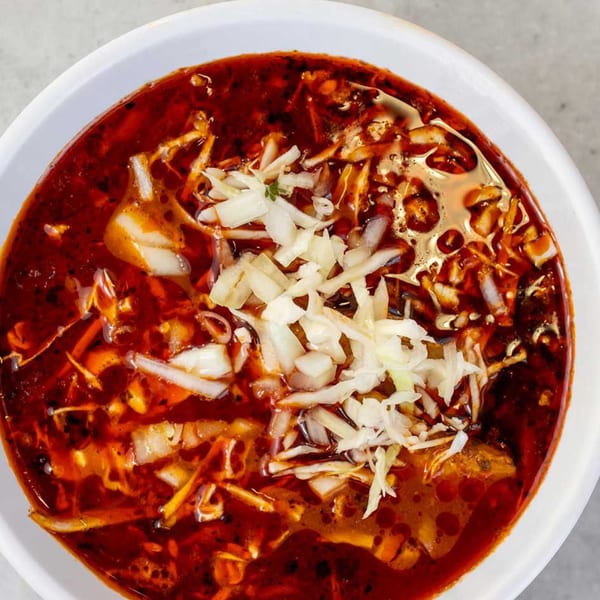 Close-up of a bowl of Giliberto's Mexican red menudo soup, topped with shredded cabbage and onions.
